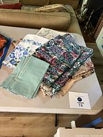 Display of three floral tablecloths and a separate set of napkins with a floral tablecloth on a white table surface