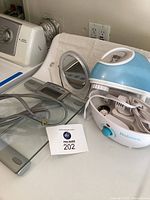 Photo showing THINNer bathroom scale, Holmes humidifier, magnifier mirror and extension cord together on a surface.