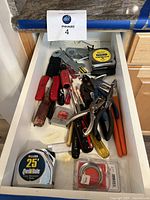 Drawer containing assorted hand tools including screwdrivers, wrenches, pliers, and tape measures.