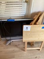 Sharp Aquos 32-inch flat TV partially obscured by three wooden TV trays stacked in front of it on a hardwood floor.