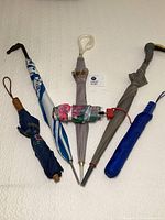 Photo showing all six umbrellas arranged flat, highlighting three long umbrellas with curved handles and three compact umbrellas, partially folded.