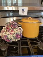 Yellow large San Ignacio soup pot with lid on kitchen stove next to white ceramic tea pot with floral fabric cozy.