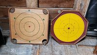 Photo of two vintage crokinole boards side by side, showing front designs and wear.