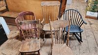 Photo showing all five antique wooden chairs grouped together on a wooden floor against a wooden wall