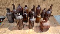 Front view of 14 amber brown glass bottles of various sizes and shapes, placed on a wooden surface.