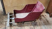 Front view of the antique child's sleigh, showing red painted wood and metal runners on a wooden floor.