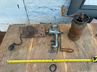 Wide view of three antique grinders on wooden surface with measuring tape showing size.