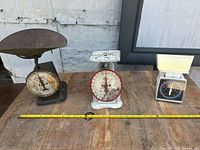 Three antique scales on wooden surface side by side: large metal platform scale, smaller kitchen scale, small modern scale