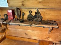 Wide shot of wooden shelf with antique pulley blocks, metal hooks, a large hook, and a coarse rope.