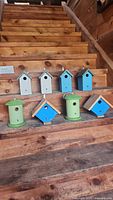 Eight wooden decorative birdhouses arranged on wooden steps, showing all items