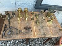 Overview photo showing the entire lot on a wooden table against a brick wall including brass candle holders, sconces, a brass bucket, and a metal wall bracket.