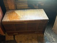Side angle view of the cedarwood chest showing its hinged top and wood grain finish with visible wear and discoloration.