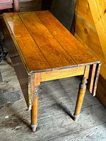 Wooden rectangular table with drop leaves on both sides, turned legs, and showing signs of wear and age.