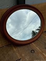 Full view of the round wall mirror with visible walnut frame and reflective surface outdoors.