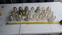 Overview of 20 old glass insulators of various sizes arranged in rows on a white table, showing different shapes and some discoloration.