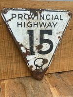 Front view of the triangular Provincial Highway 15 road sign showing text and rust wear.