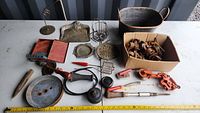 Photo of assorted vintage tools, pulleys, kitchenware and hardware items laid out on white table against dark background.