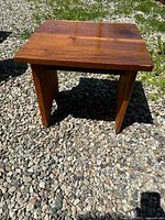 Small rectangular wooden table with visible grain and wear, placed on gravel