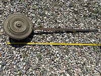 Full view of the vintage bed warmer placed on gravel showing the metal lid with decorative holes and long handle.