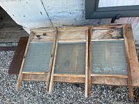 Three wooden frame glass washboards laid side by side on gravel surface outside, showing tops and glass ridges.