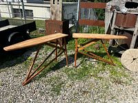 Two wooden ironing boards with metal support frames outdoors on gravel.