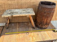 Rustic wooden stool next to wooden barrel on wooden surface with measuring tape showing stool size.