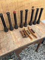 Front view of the lot including 11 wool spinner bobbins and 4 weaving shuttles placed on rustic wooden surface with a wooden backdrop.