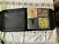 Black CD binder open flat on table with 3 visible clear sleeves containing 5 CDs on right and 2 CDs on left side with empty slots.