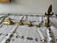 All four brass loon family figurines and the brass flag pole topper arranged in a row on a white cloth with brown patterns.