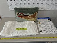 Hooked canoe throw pillow and folded white queen duvet cover with a subtle pattern laid on tabletop with ruler