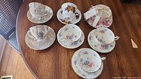 Overview of six different porcelain teacups and saucers with various floral designs displayed on a wooden table.