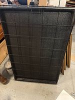 Black metal dog cage folded flat showing plastic bottom tray and metal wire sides, stored against wall.