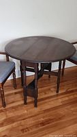 Full view of round wooden drop leaf table with spindle legs on hardwood floor next to chairs
