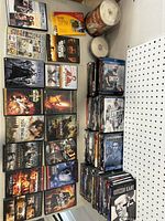 Photo showing multiple DVD cases stacked side by side and some flat. Includes titles like Star Wars, The Matrix, Pirates of the Caribbean, Kodak photo paper, and a spindle of blank DVDs.