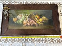 Full view of fruit painting framed in wood with metal grape decoration, showing overall condition and size reference with measuring tape.