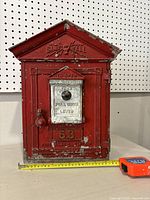 Front view showing full facade with embossed logo, lever plate, number marking and tape measure at base.