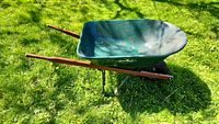 Full side view of Garant green metal wheelbarrow with wooden handles and black tire on grass.