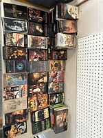 Wide shot showing a variety of vintage VHS tapes stacked on a shelf, titles visible include The Exorcist, Spawn, The Crow, The Outlaw Josey Wales, Battle of Britain among others.