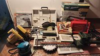 View of assorted power tools including cordless drill box, belt sander, orbital sander, saw blades, and staple gun.