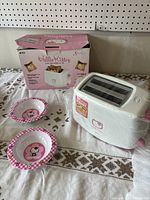 Retro Hello Kitty two-slot toaster with its original box and two small Hello Kitty plates on a tablecloth background.