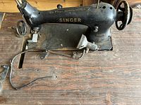 Close-up of the Singer industrial sewing machine mounted on the wooden table, showing machine's top surface, needle area, and the Singer branding.