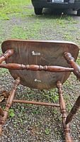 Photo of the underside of an antique wooden armchair, showing turned spindle legs and metal brackets on the brown wooden seat bottom.