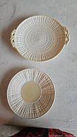 Two cream-colored plates with an embossed woven pattern, one dinner plate with handles, one smaller plate