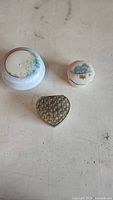 Photo showing top view of three jewelry boxes: two round porcelain boxes with floral designs and one heart-shaped metal box