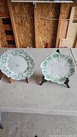 Two bone china plates on display stands, showing floral scalloped design and white base