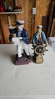 Two ceramic nautical sailor figurines placed on a table in a wooden indoor setting.