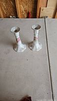 Pair of white porcelain candlestick holders with pink flower design, standing on a table in a workshop.