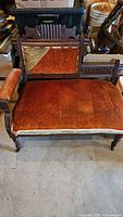 Front view of Victorian antique settee showing ornately carved wooden frame, reddish velvet seat cushion with moderate wear.