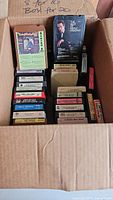 Photo of a cardboard box containing a collection of vintage 8-track tapes featuring country music artists from the 1970s-1980s era.