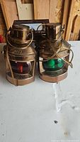 Pair of vintage brass nautical lanterns with red and green lenses labeled Port and Starboard placed on white surface.